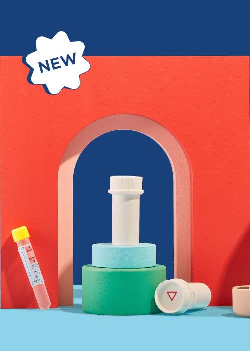 Wisp pill vials, testing tubes and a hand holding a testing pipette with colorful abstract shapes on a blue surface