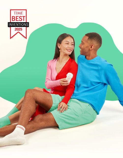 A woman wearing a pink and red dress is handing a Wisp medication bottle to her partner who is wearing a blue shirt and green shorts