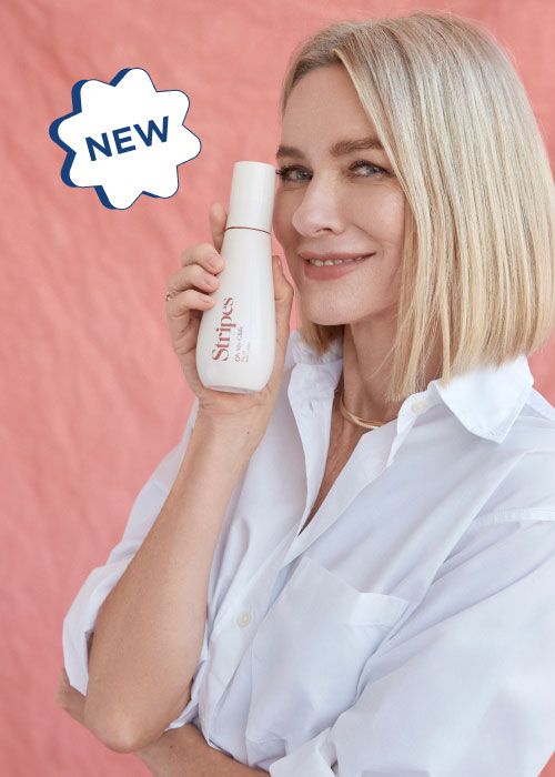 Naomi Watts - Founder of Stripes Beauty wearing a white shirt while holding a Stripes Beauty product in front of a pink background