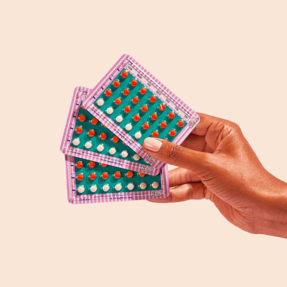 Birth Control packets in a person's hand on a cream backgound