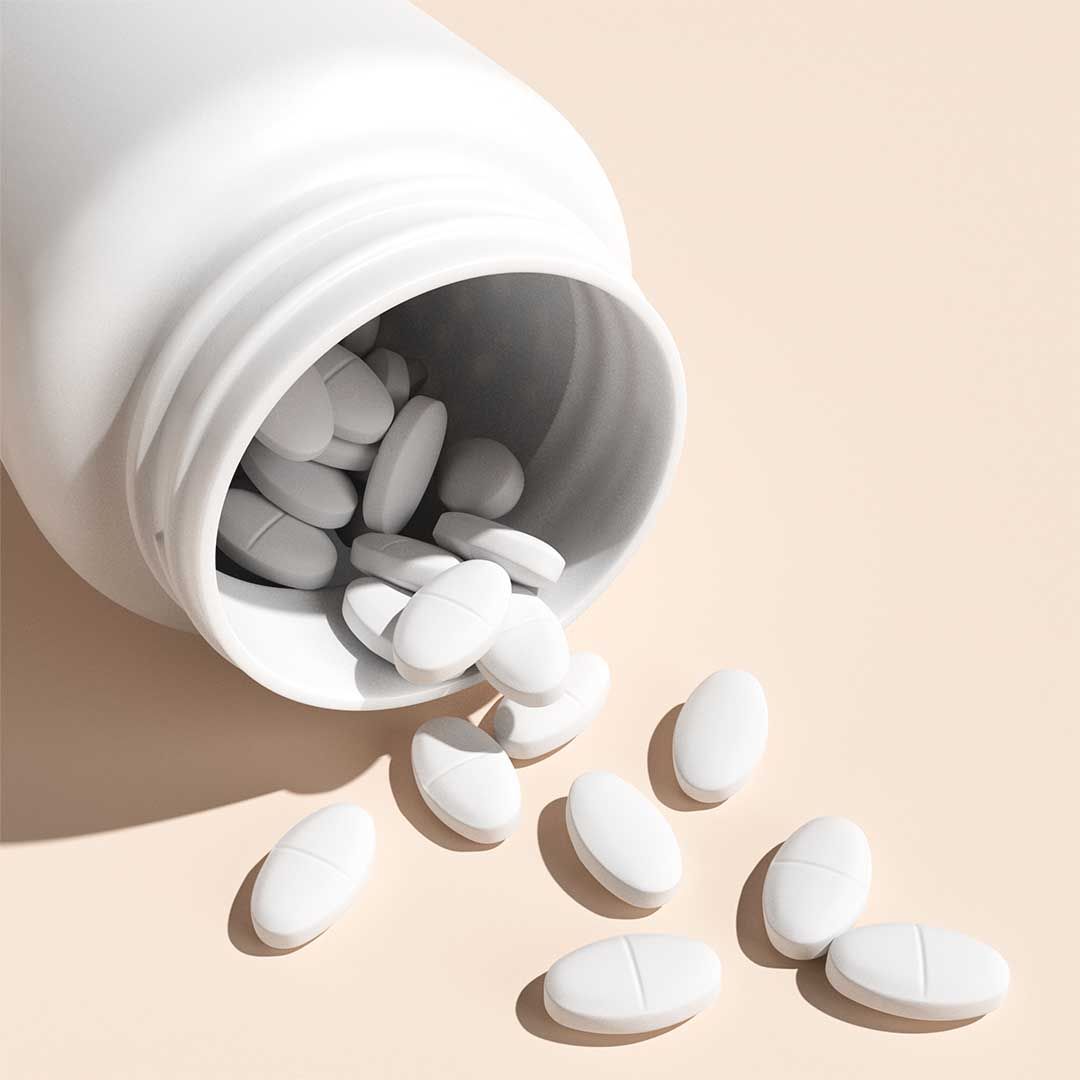 A white bottle has small white pills spilling out of it on a cream surface