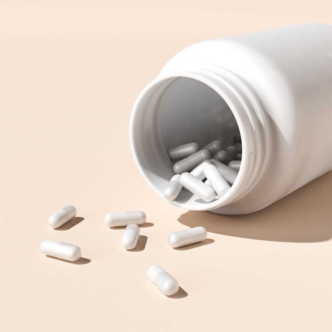 White capsules spilling out of a white bottle on a cream surface