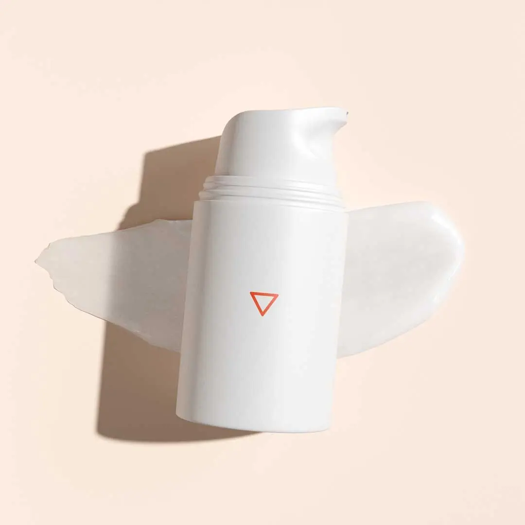 A cream swatch and a pump bottle on a cream surface
