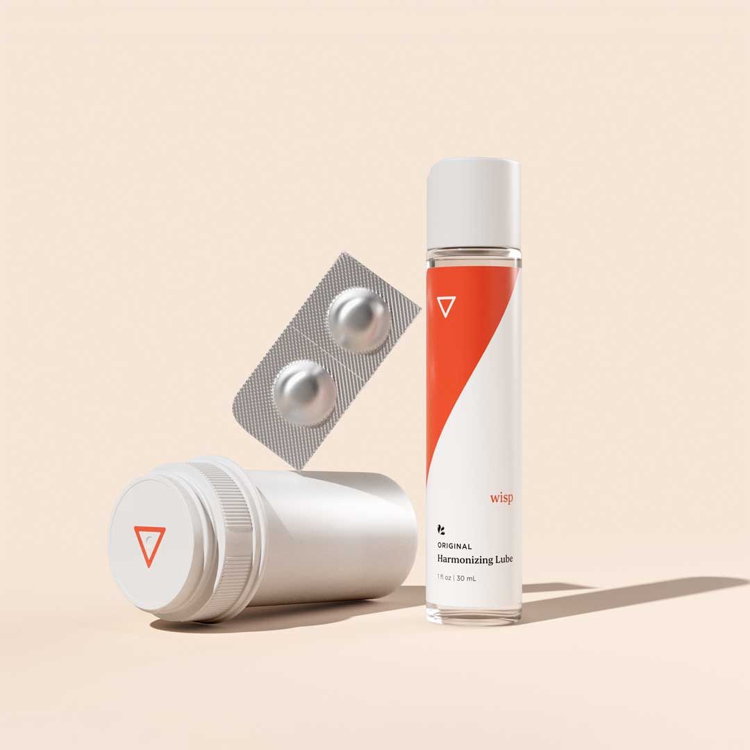Wisp Harmonizing Lube, a pill packet and a pill bottle on a cream surface
