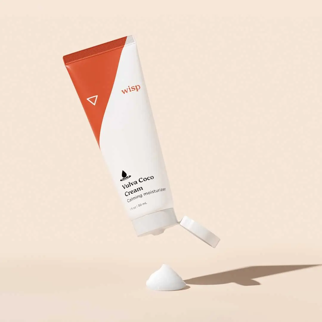 A bottle of Wisp Vulva Coco Cream with a dollop of cream on a beige surface