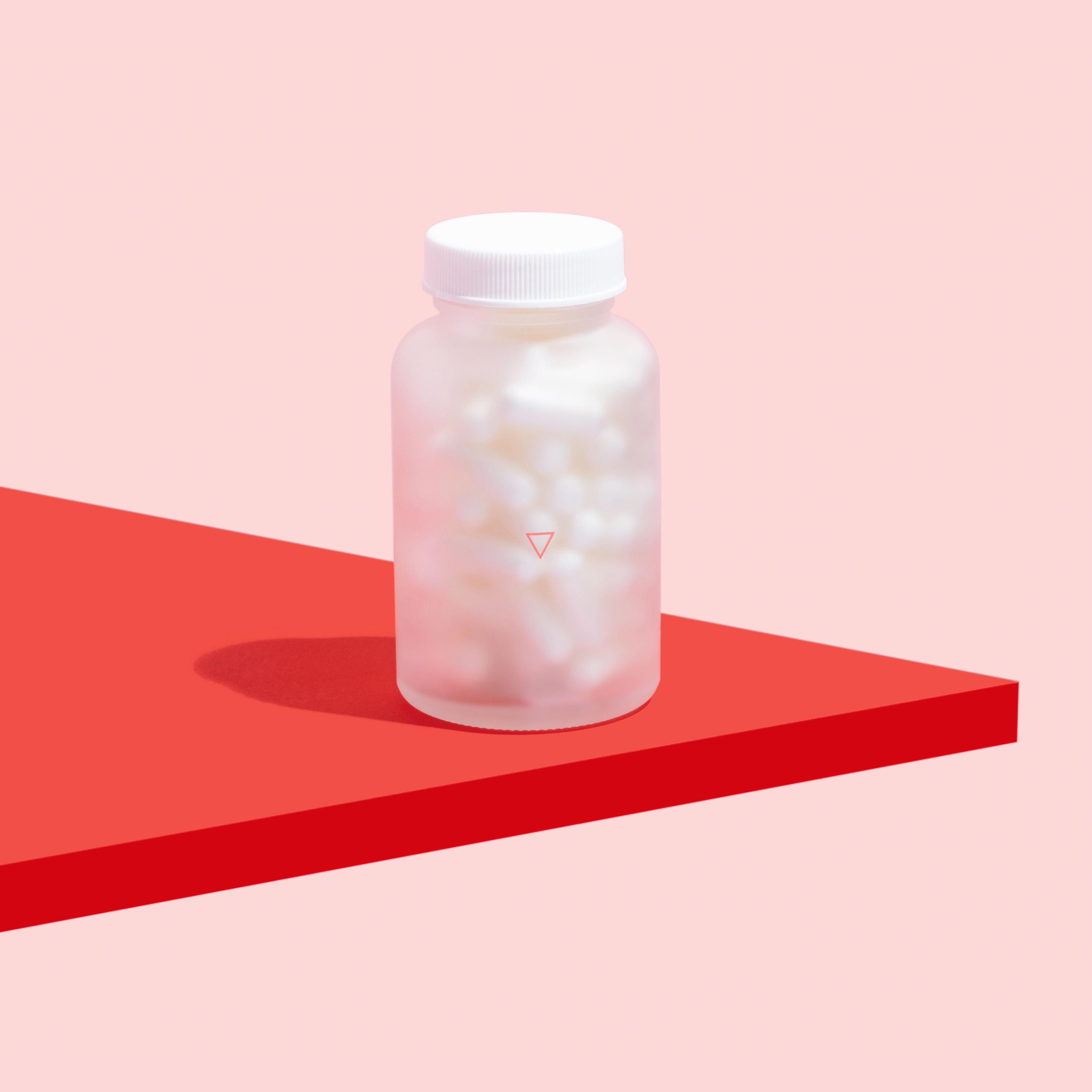 Bottle of Valacyclovir to treat oral and genital herpes outbreaks on a red surface, on a pink background